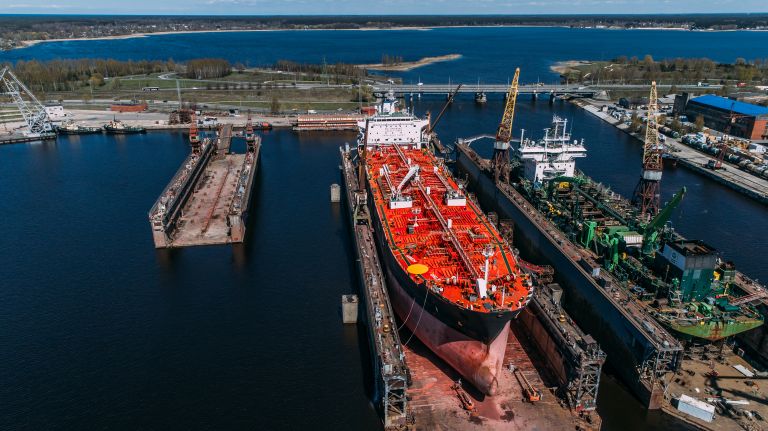 Large commercial vessel in drydock surrounded by cranes and marine equipment, ready for maintenance or parts resale